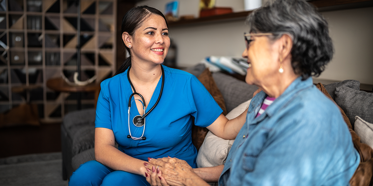 A woman receiving nursing care at home in Saginaw holds the hand of her nurse and smiles.