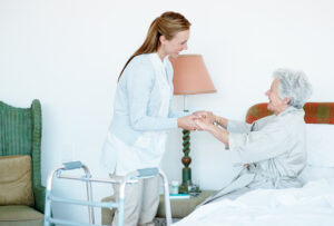 A caregiver utilizes safe lifting and transferring techniques to help an older woman out of bed.