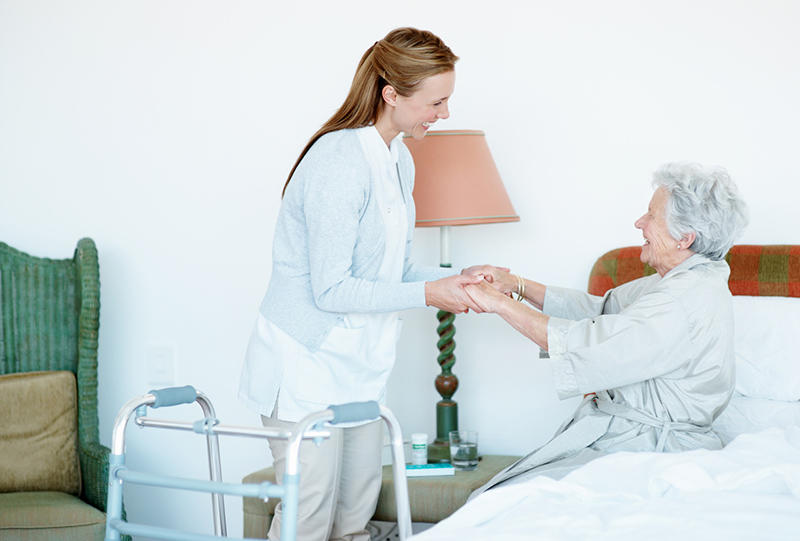 A caregiver utilizes safe lifting and transferring techniques to help an older woman out of bed.