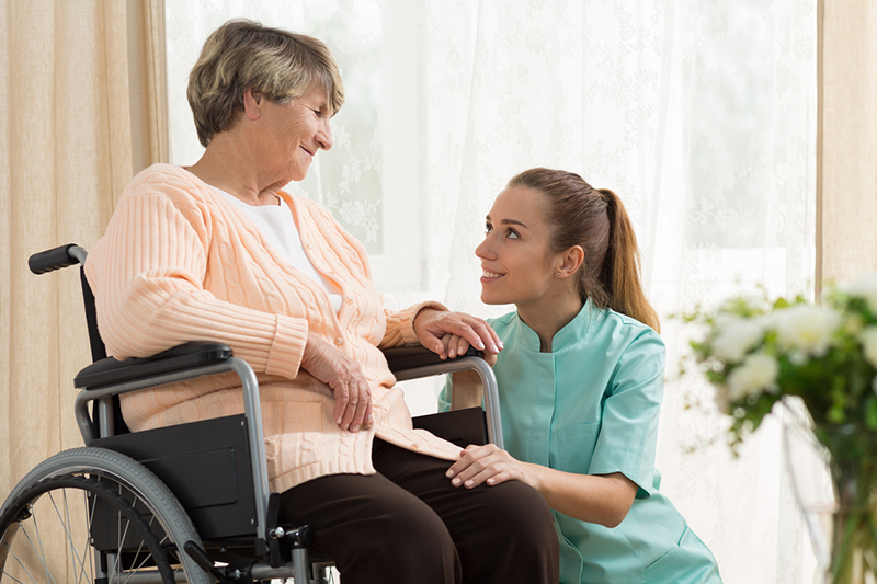 A woman who knows how to prevent a caregiving injury prepares to help an older woman transfer from her wheelchair.