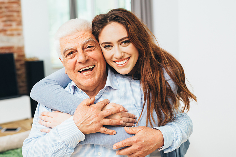 A woman who has learned to feel more confident as a caregiver hugs her dad as they both smile.