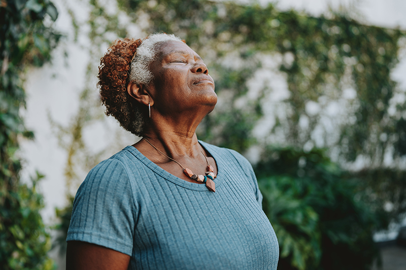 A woman at risk for caregiver burnout closes her eyes and breathes deeply while enjoying the outdoors.