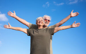 An older couple raise their arms to the sky, smiling at their newfound freedom from chronic pain.