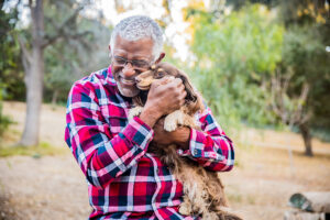 A man laughs as he cuddles with his dog, who helps him live a better quality of life with a chronic disease.