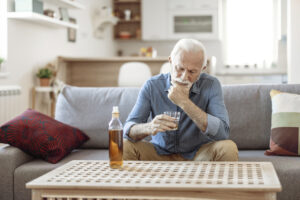 An older man, one of many impacted by substance misuse in older adults, stares sadly into his glass of whiskey.