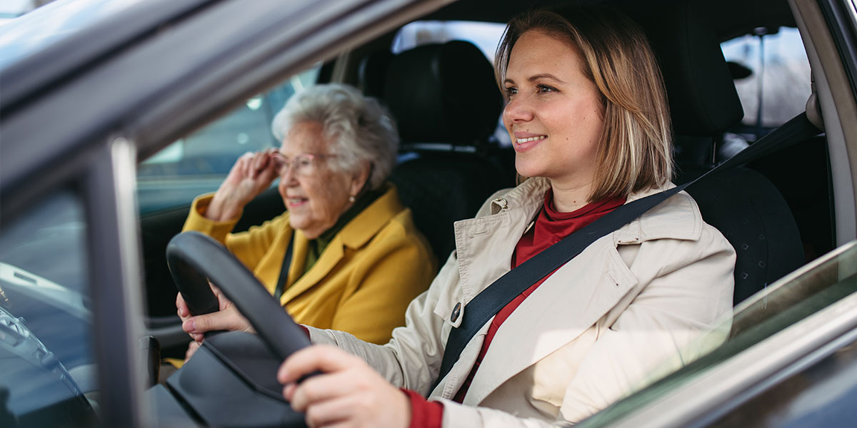 A caregiver provides senior transportation services in Saginaw to a smiling older woman.