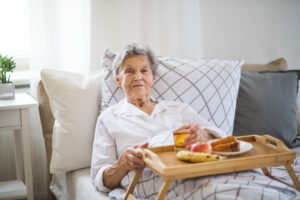 An older woman experiencing eating changes at the end of life sits in bed with a tray of uneaten food.