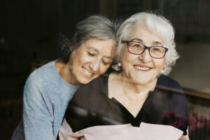 A woman who has learned how to become a better dementia caregiver smiles as she hugs her mom.