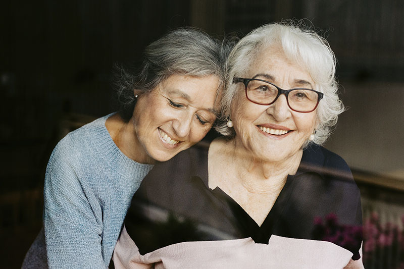 A woman who has learned how to become a better dementia caregiver smiles as she hugs her mom.