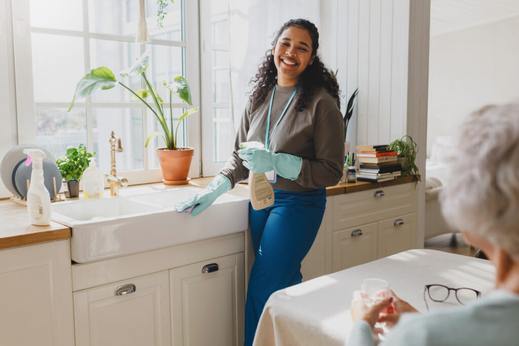 A caregiver cleans an older woman’s kitchen after helping her debunk common myths about home care.