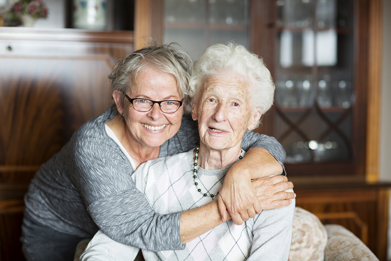 An older woman experiencing some of the challenges that come with aging receives a hug from her daughter.